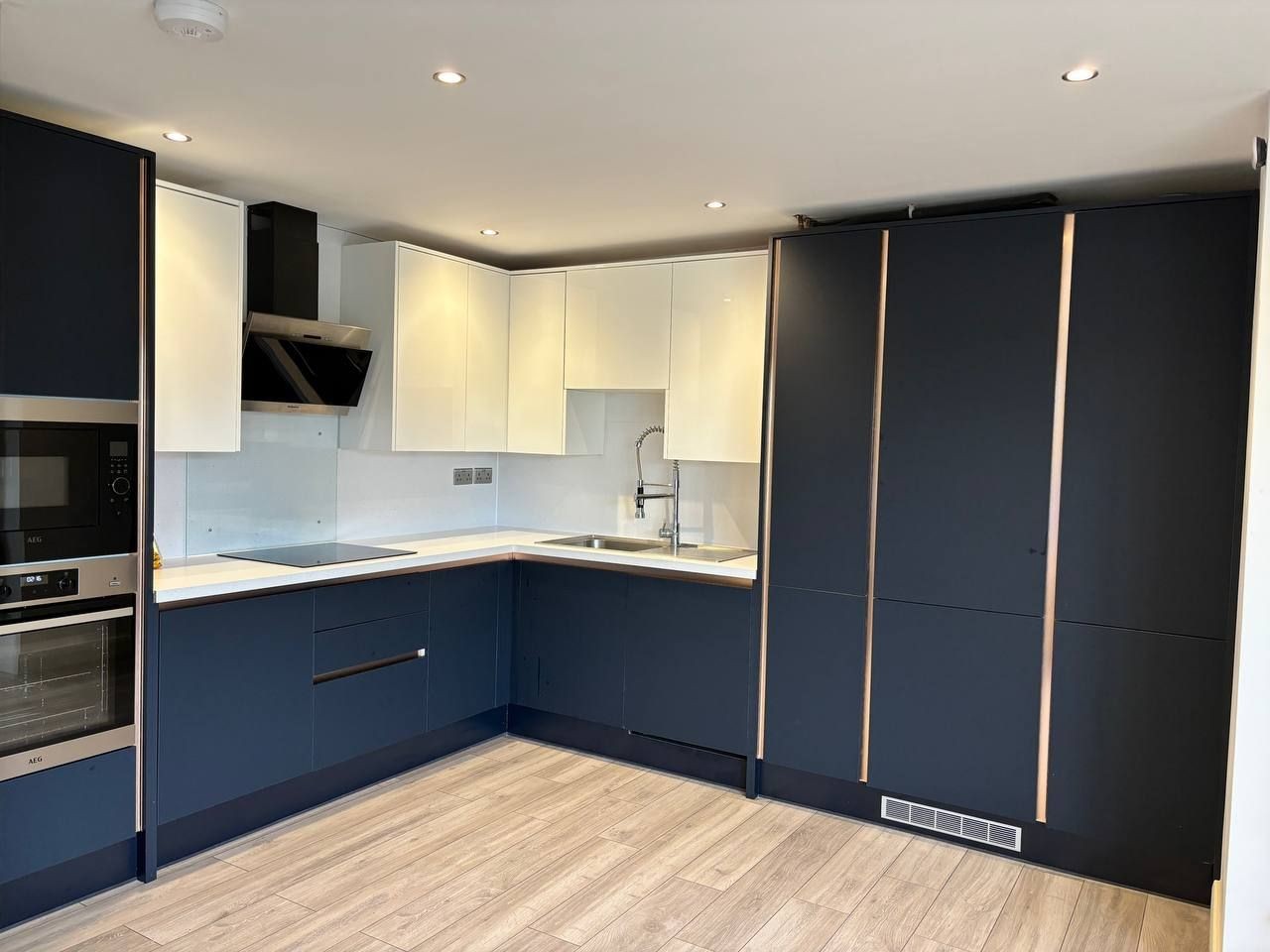 Modern kitchen with navy and white cabinetry, stainless steel appliances, and wooden flooring.